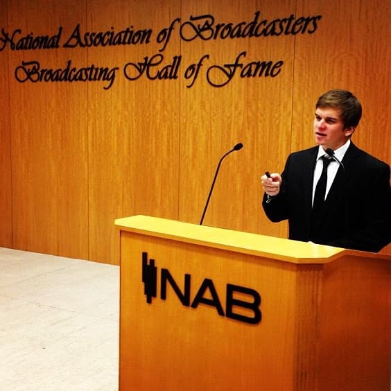 Our founder speaking at a podium marked NAB, in front of a wall that reads National Association of Broadcasters Broadcasting Hall of Fame